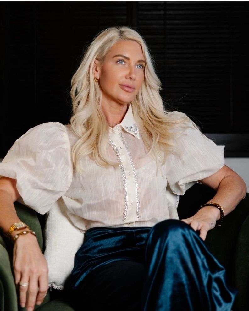 Heather Hellmann in a white blouse and dark velvet trousers, seated.